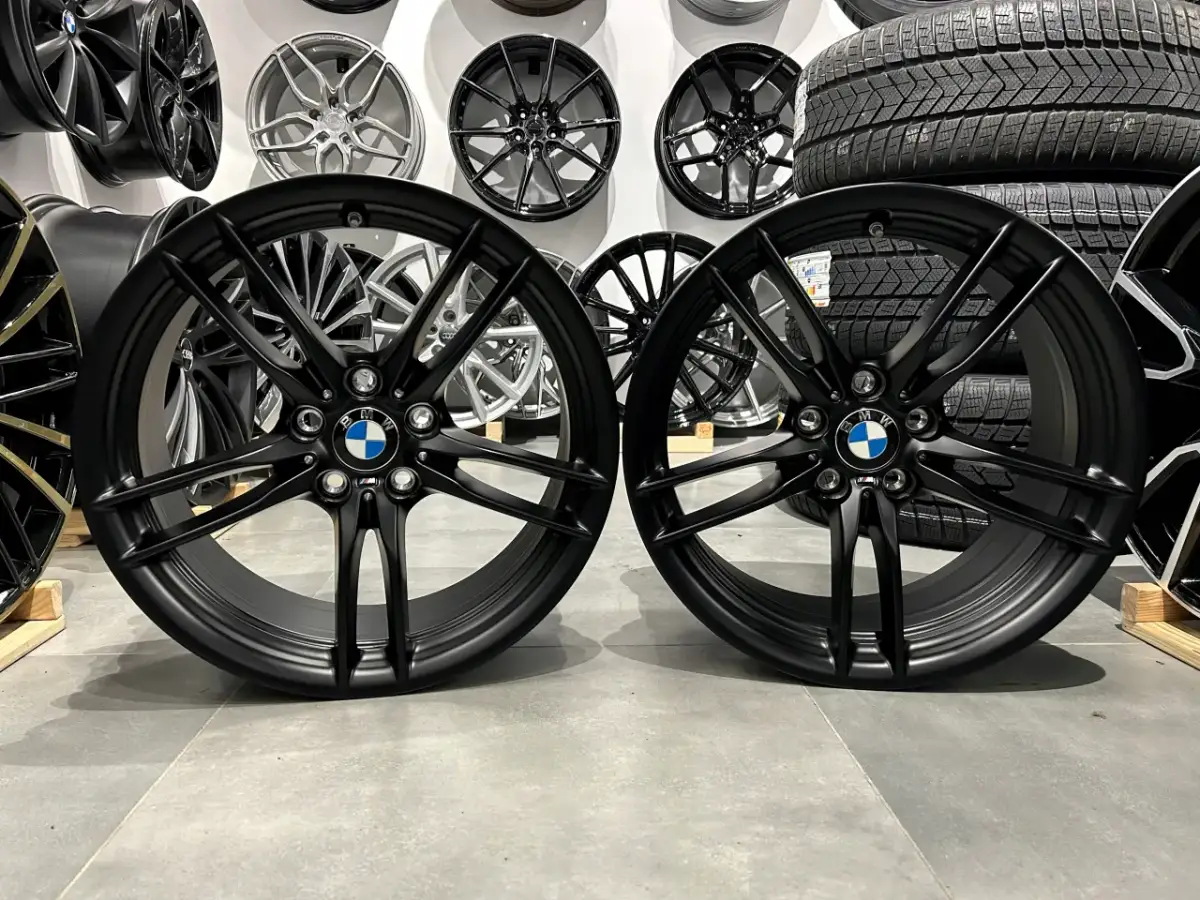 Dwa czarne felgi BMW z logo, idealne do tuningu. W tle inne felgi i opony.