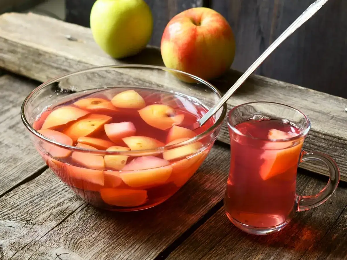 Szklanka i miska pełne pysznego, domowego kompotu z jabłek, obok świeże owoce.