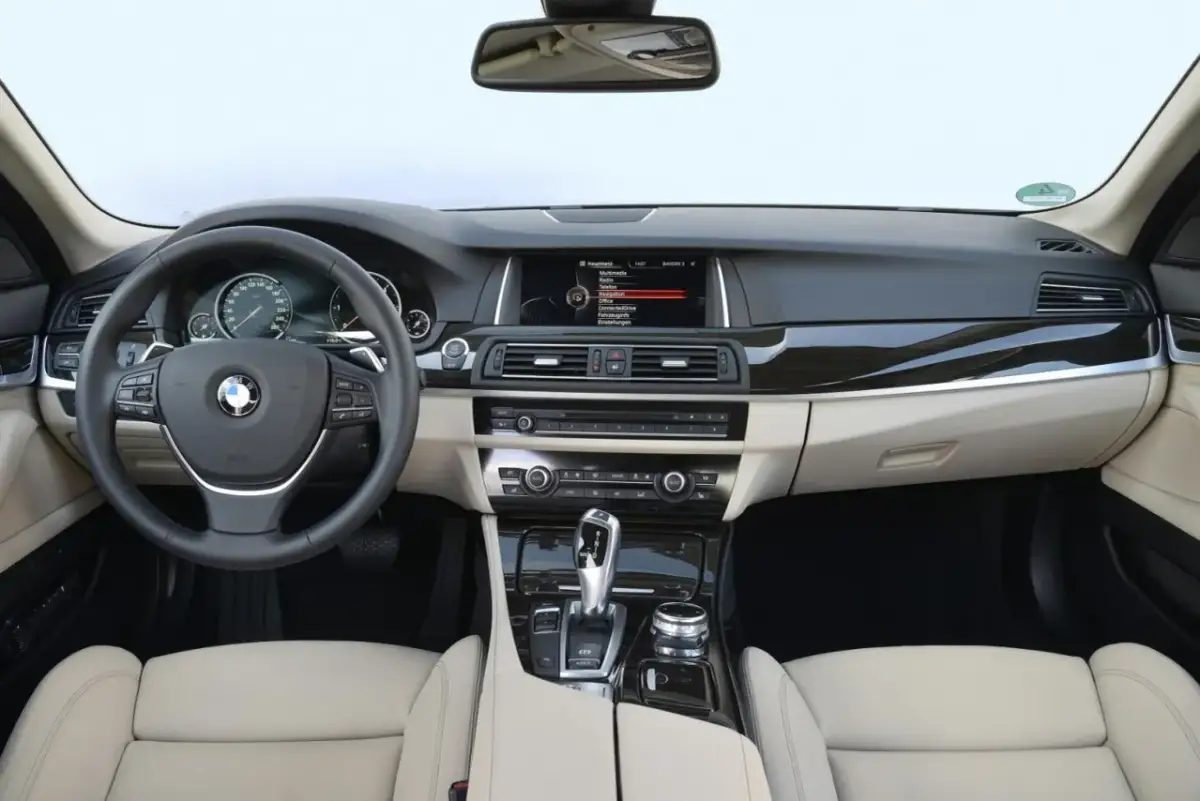 Wnętrze BMW F10 z jasną tapicerką, kierownicą, ekranem multimedialnym i panelem środkowym.