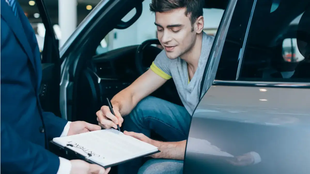 Mężczyzna w samochodzie podpisuje umowę. Chcesz wiedzieć, jak sprawdzić, czy auto jest w leasingu? Dokumenty są kluczem.