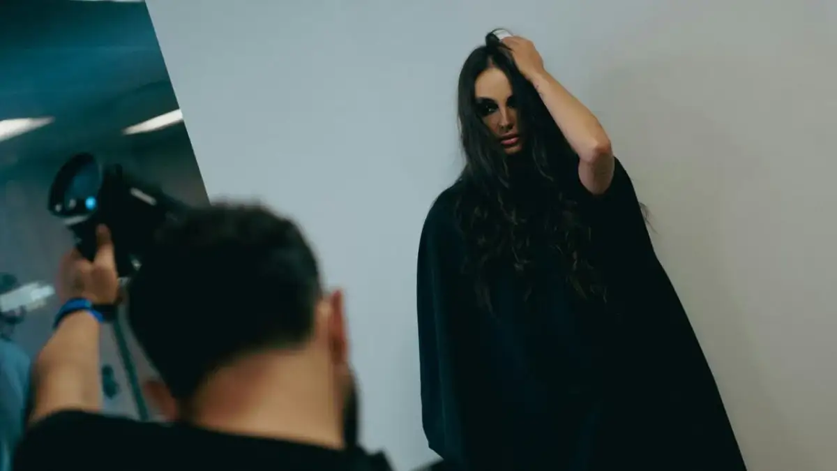 Modelka z mocnym makijażem pozuje do zdjęcia, fotograf trzyma aparat.