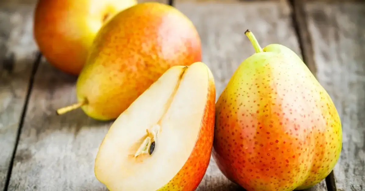 Gruszka właściwości: soczysta, słodka, pełna witamin. Na drewnianym blacie leżą całe i przekrojone gruszki.