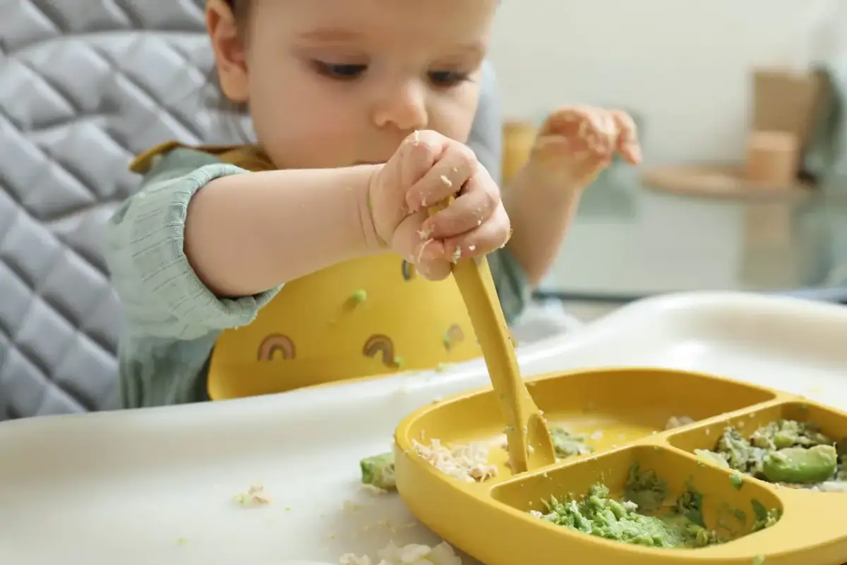 Dziecko próbuje samodzielnie jeść, chwytając widelczyk. Zastanawiasz się, ile razy w tygodniu mięso dla niemowlaka?