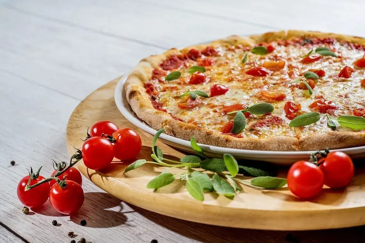 Pizza z pomidorkami koktajlowymi i bazylią na drewnianej desce.