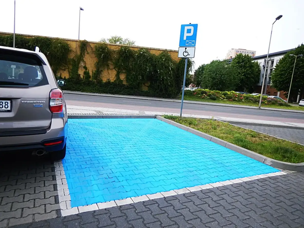 Niebieski, specjalny obszar do parkowania na miejscu dla niepełnosprawnych. Obok znak drogowy P i symbol wózka inwalidzkiego.