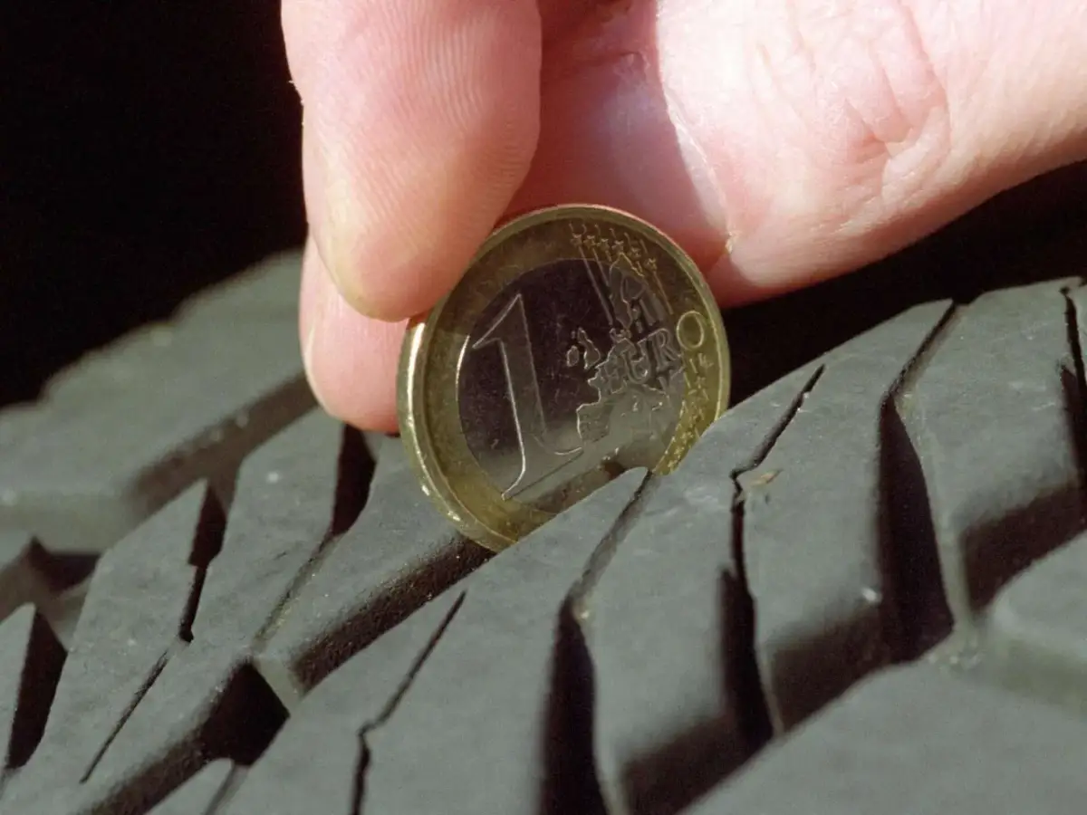 Daumen und 1-Euro-Münze messen Reifenprofiltiefe.