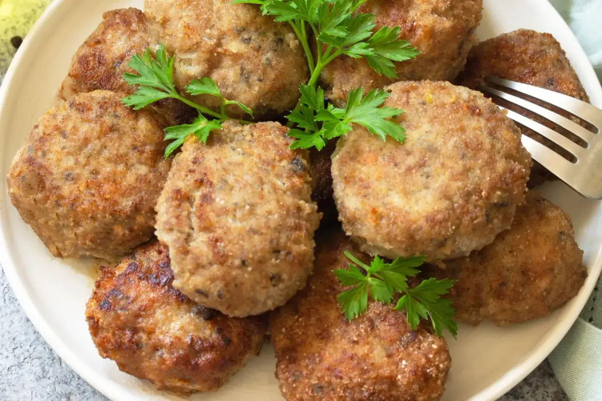 Kotlety mielone z natką pietruszki na talerzu, obok widelca.