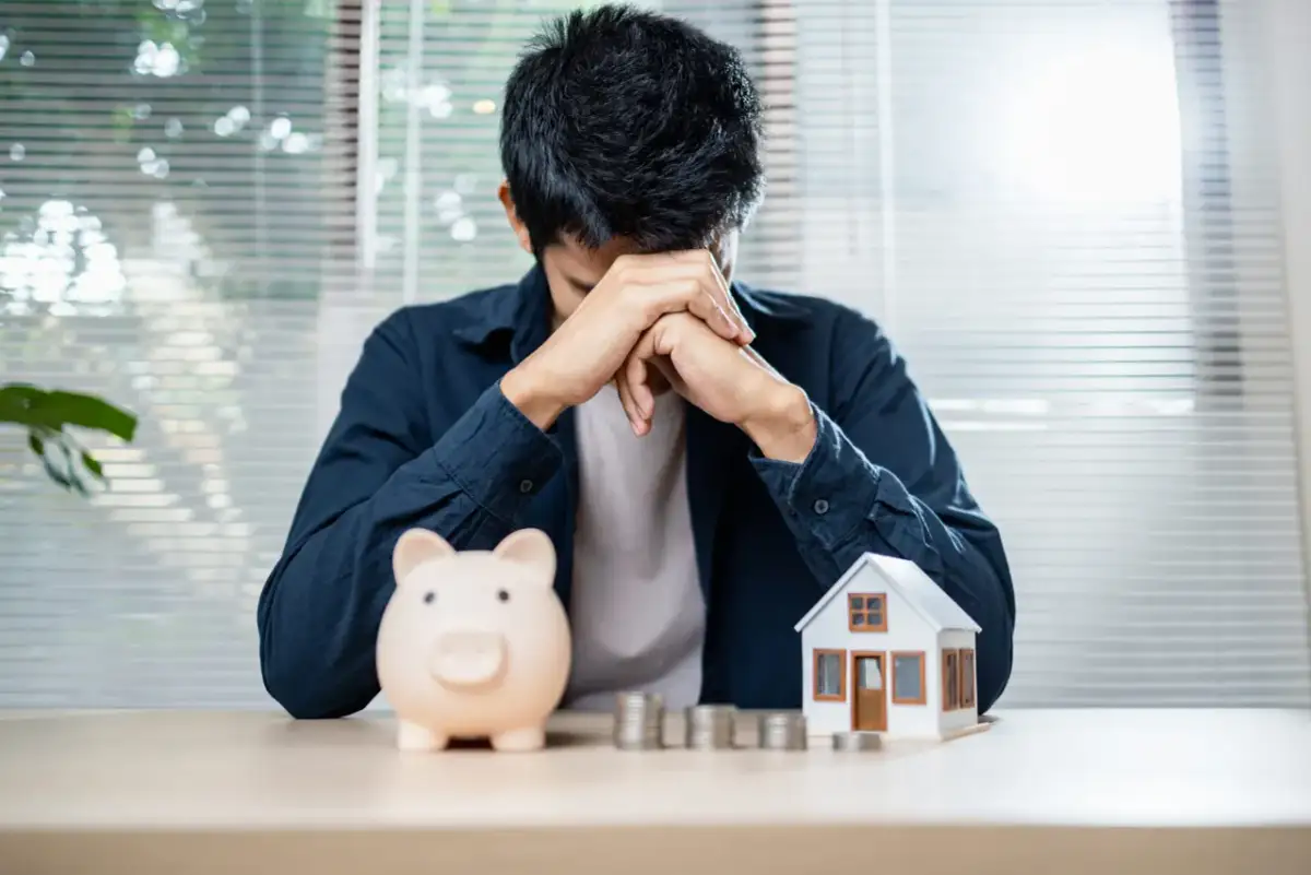 Zmartwiony mężczyzna z domkiem i skarbonką. Czy to pożyczka na dom?