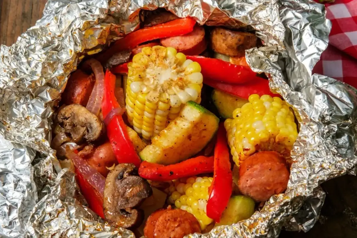 Pyszne sakiewki na grilla z kukurydzą, papryką, pieczarkami i kiełbasą, zapakowane w folię aluminiową.