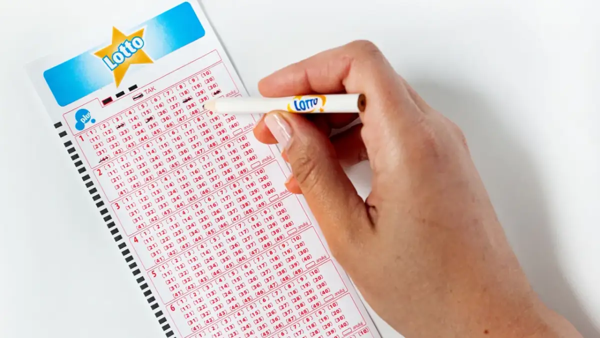 Dłoń z ołówkiem zaznacza liczby na kuponie gry Lotto.