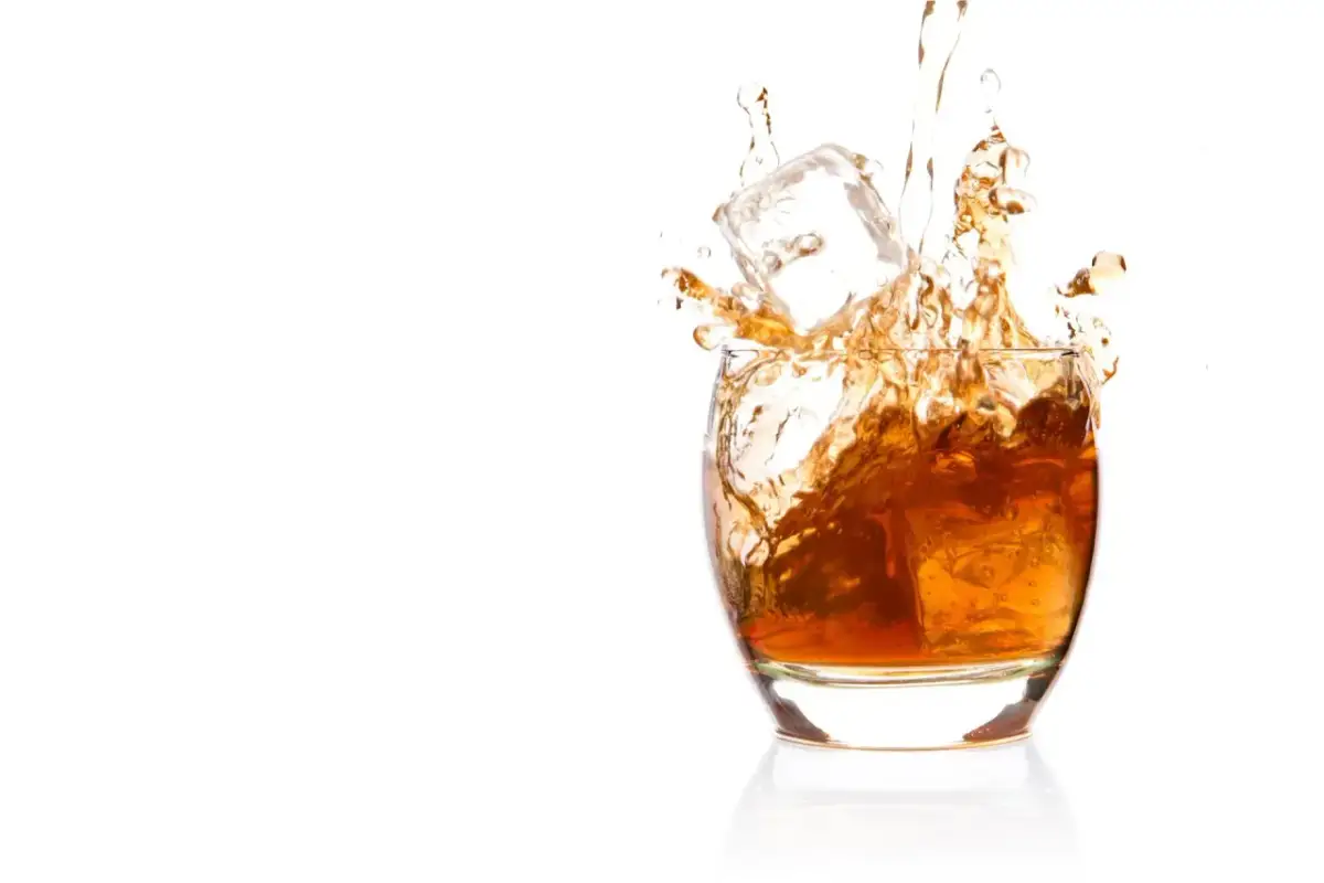 Bursztynowa whisky z lodem rozpryskuje się w szkle. Czy whisky podnosi ciśnienie? To pytanie pozostaje otwarte, gdy patrzymy na ten dynamiczny obraz.