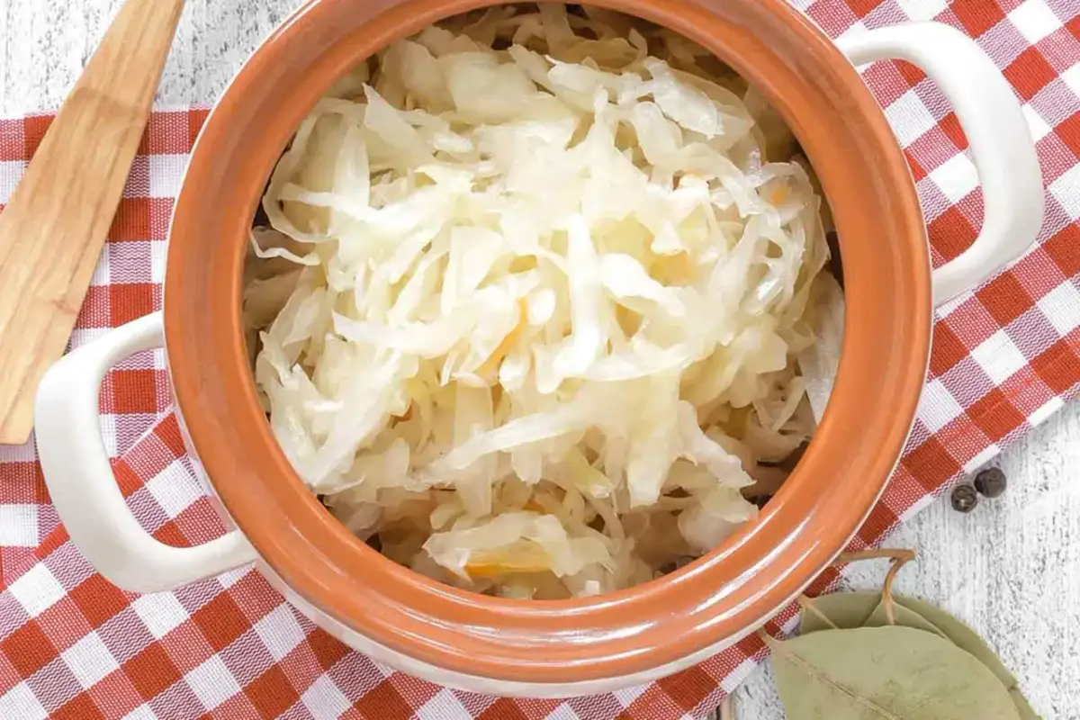 Sauerkraut in einem Tontopf mit kariertem Tuch, Lorbeerblättern und Pfefferkörnern.