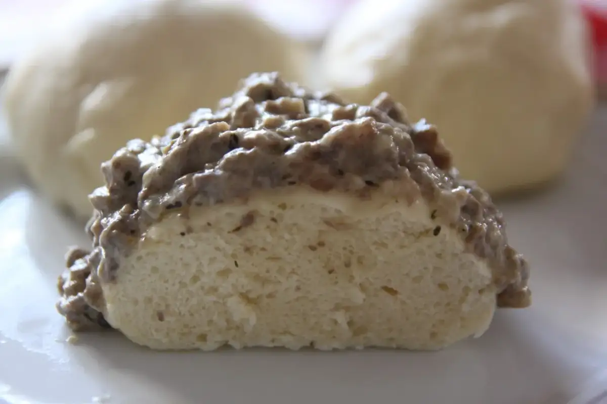 Pampuch przekrojony na pół, polany gęstym sosem mięsnym, na białym talerzu.