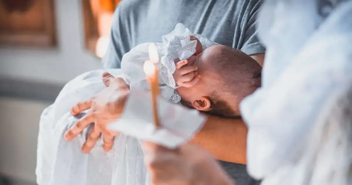 Dziecko w białej szacie trzymane na rękach, płonąca świeca.