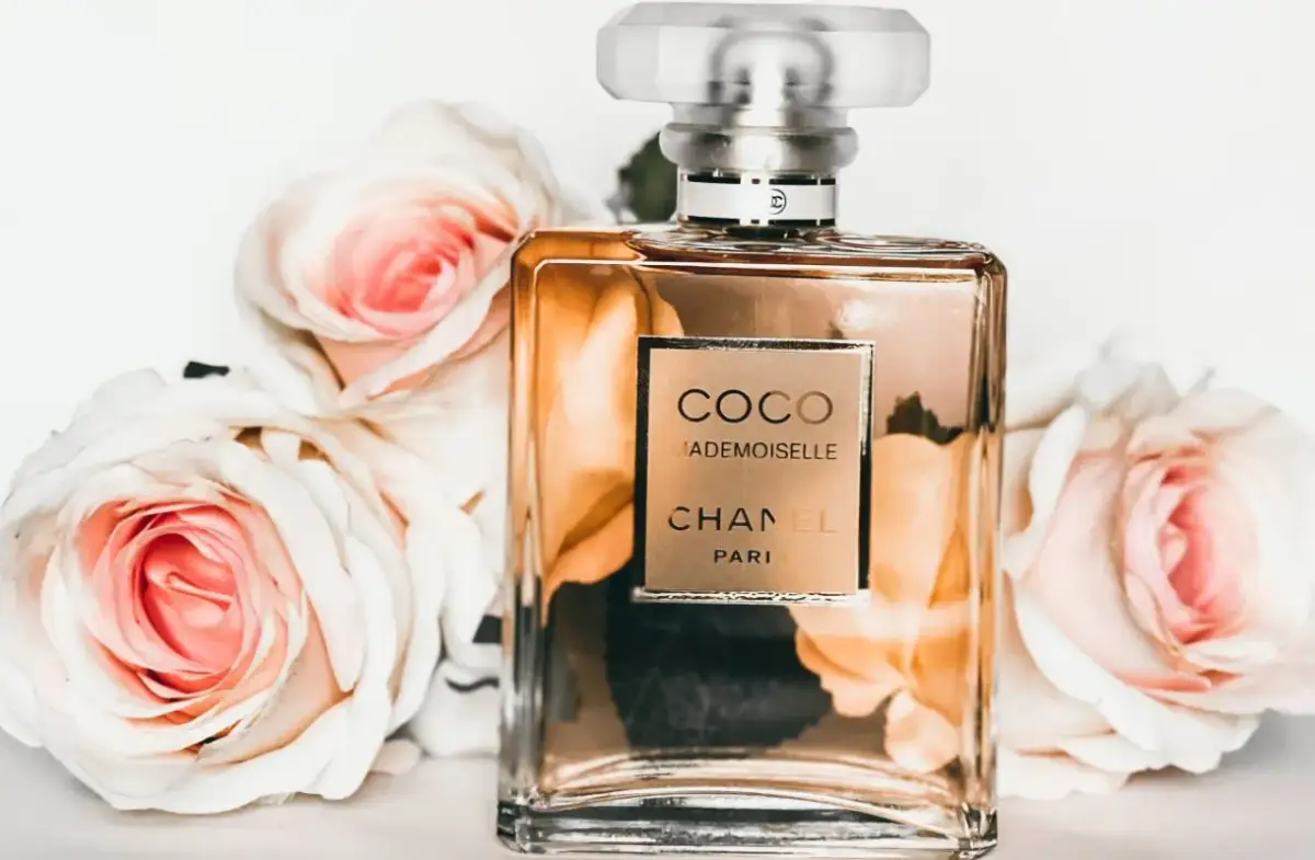 Szklana butelka perfum Chanel Coco Mademoiselle otoczona jasnoróżowymi różami.