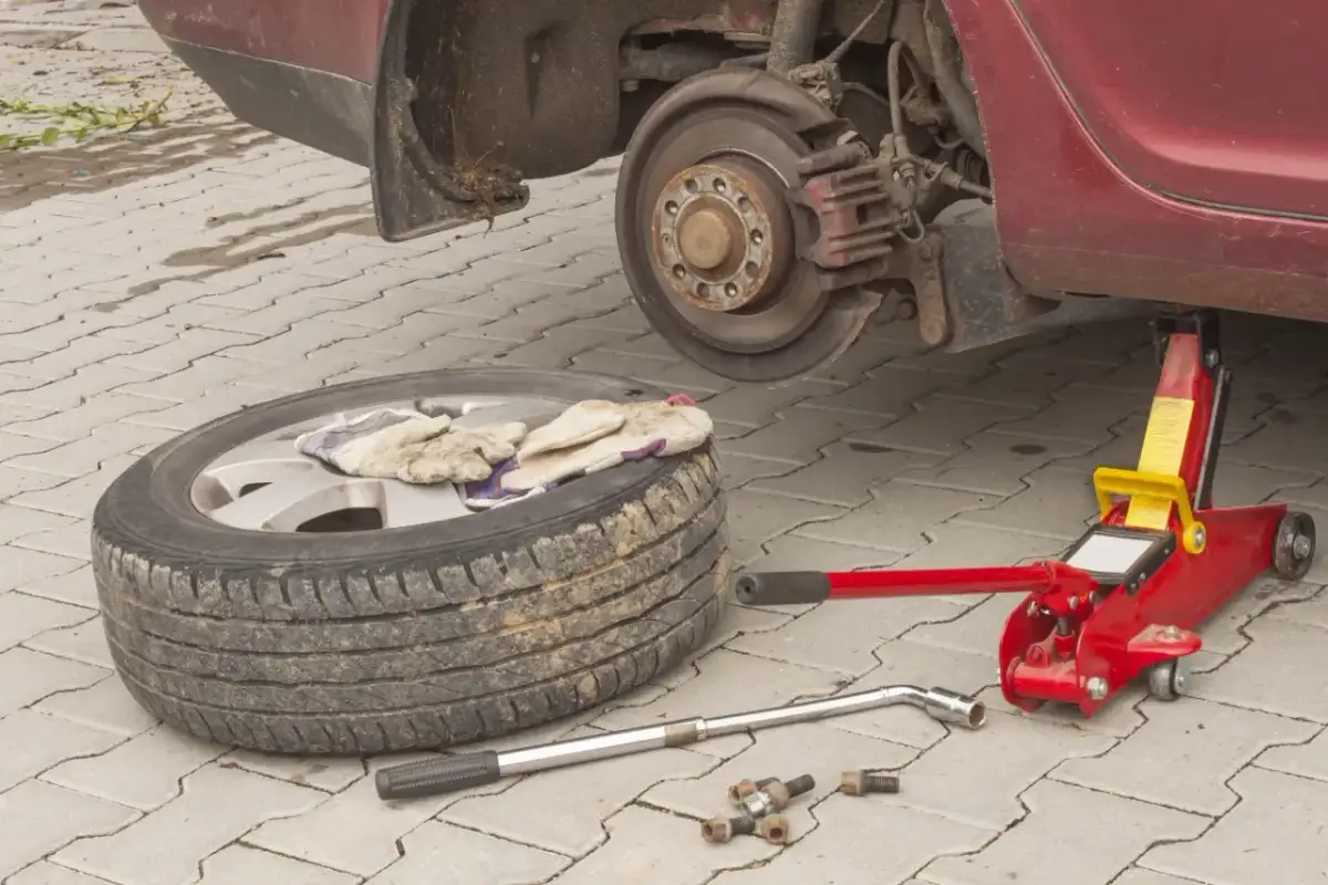 Koło zapasowe, podnośnik, klucz i śruby leżą obok podniesionego samochodu.