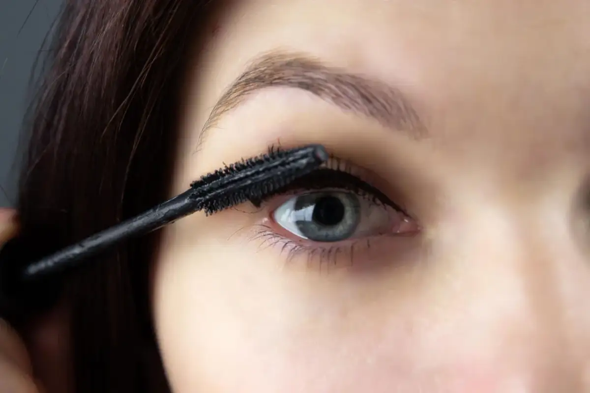 Zbliżenie na oko, na które nakładany jest tusz do rzęs czarną szczoteczką.