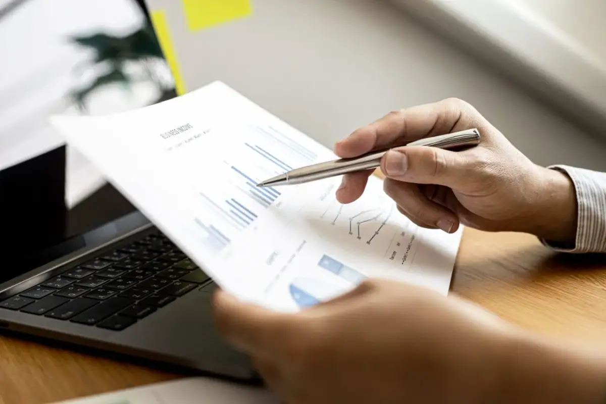 Analiza wykresów na papierze, wskazując długopisem. Skupienie na zarządzaniu kapitałem obrotowym i optymalizacji procesów.