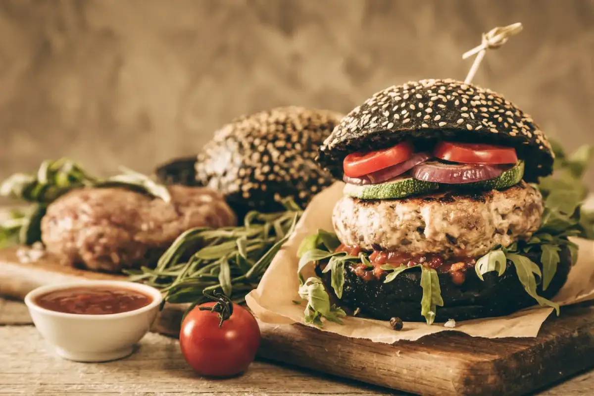 Soczysty burger z czarną bułką, kotletem, warzywami i sosem.