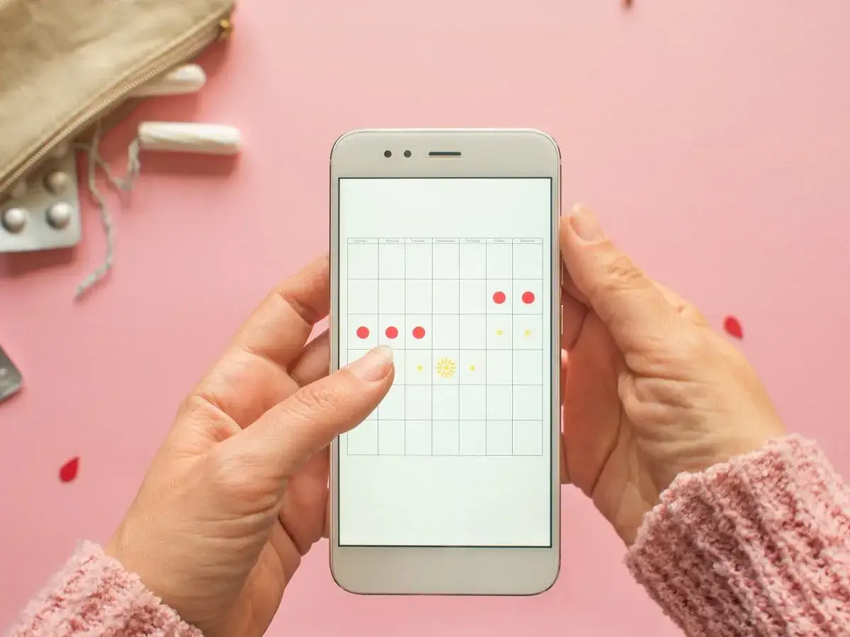 Dłoń trzyma smartfon z kalendarzem cyklu. Czy ginekolog może zbadać podczas okresu? Na ekranie zaznaczone dni miesiączki.