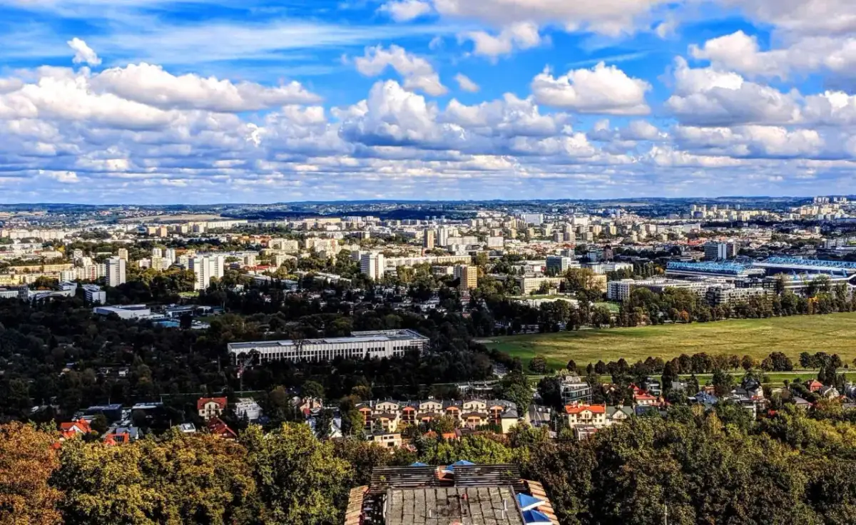 Widok na rozległe osiedla Krakowa, gdzie ceny mieszkań mogą być wysokie. W oddali widać zabudowania i zieleń.