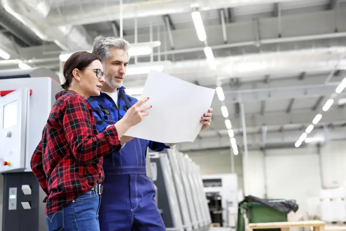 Para tworzenia instrukcji obsługi, para pracowników analizuje dokumenty w hali produkcyjnej.
