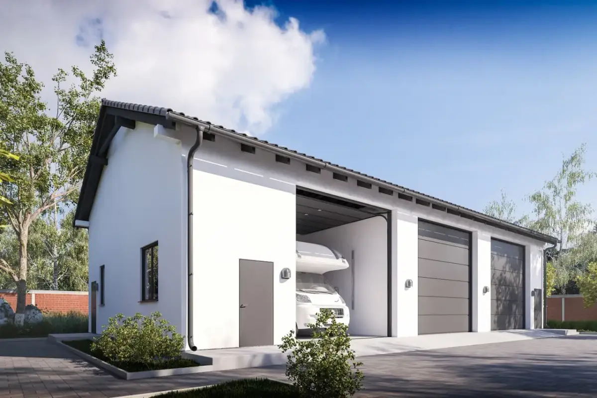 Nowoczesny budynek gospodarczy z białymi ścianami, szarym dachem i bramami garażowymi. W jednym z otworów widać kampera.