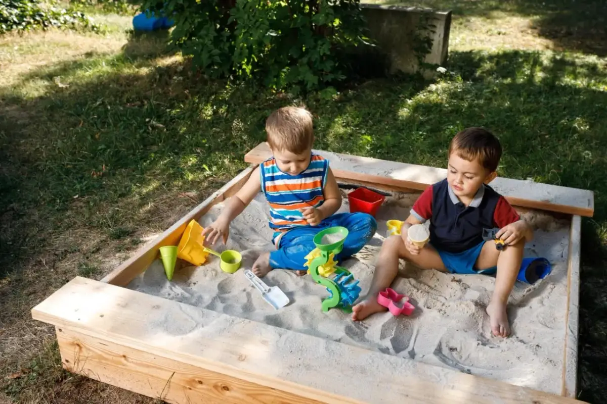 Dwóch chłopców bawi się w piaskownicy, budując zamki z piasku. To świetny sposób, jak zrobić piaskownicę i zapewnić dzieciom rozrywkę.