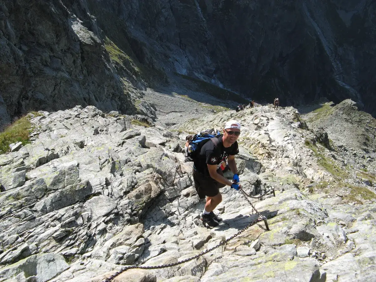Turysta pokonuje trudny szlak w Rysach, chwytając się łańcuchów.