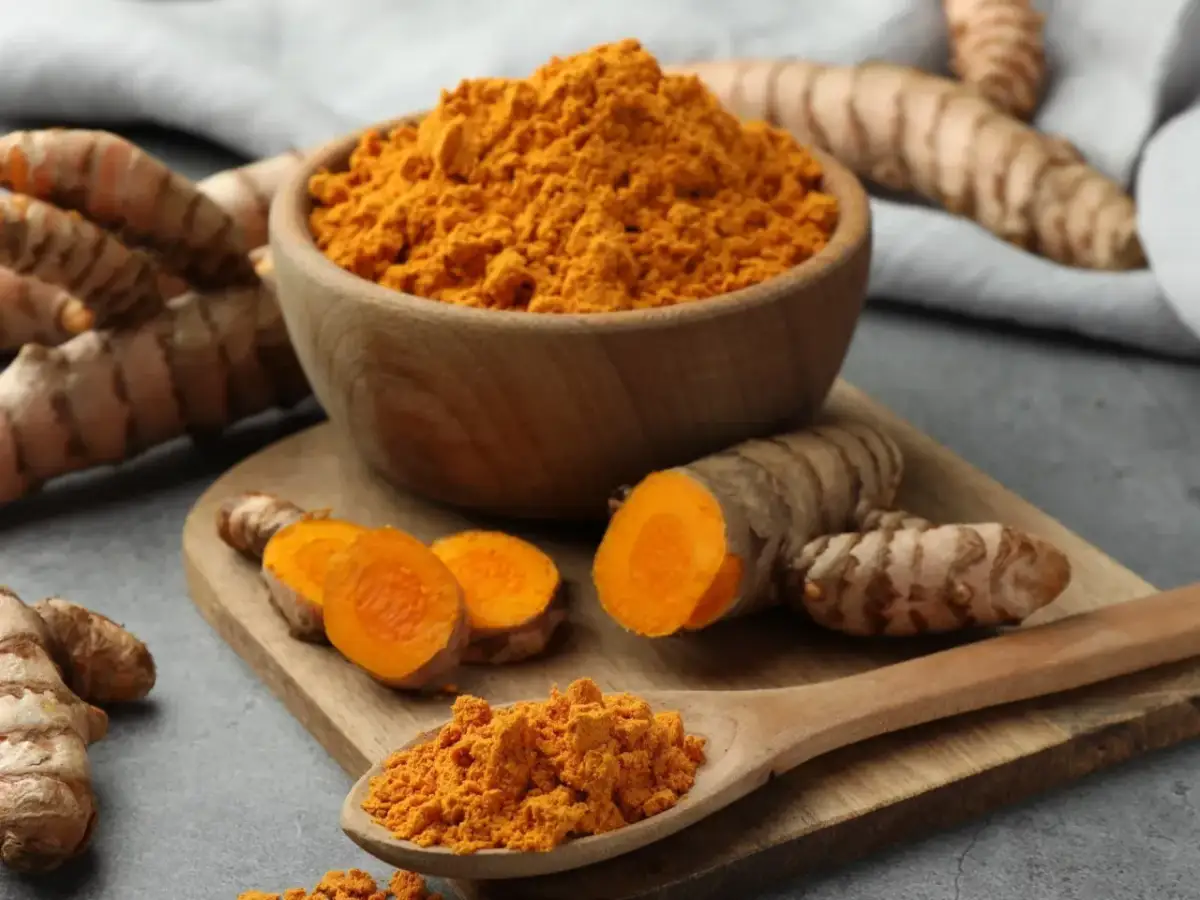 Korzeń kurkumy i mielona kurkuma w misce i na łyżce.
