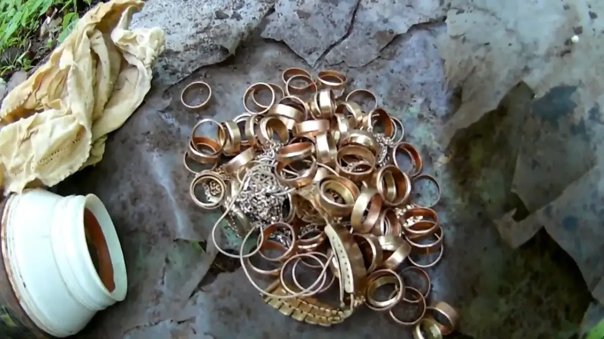 Kupa złotych pierścionków i biżuterii na ziemi, obok białego pojemnika i materiału.