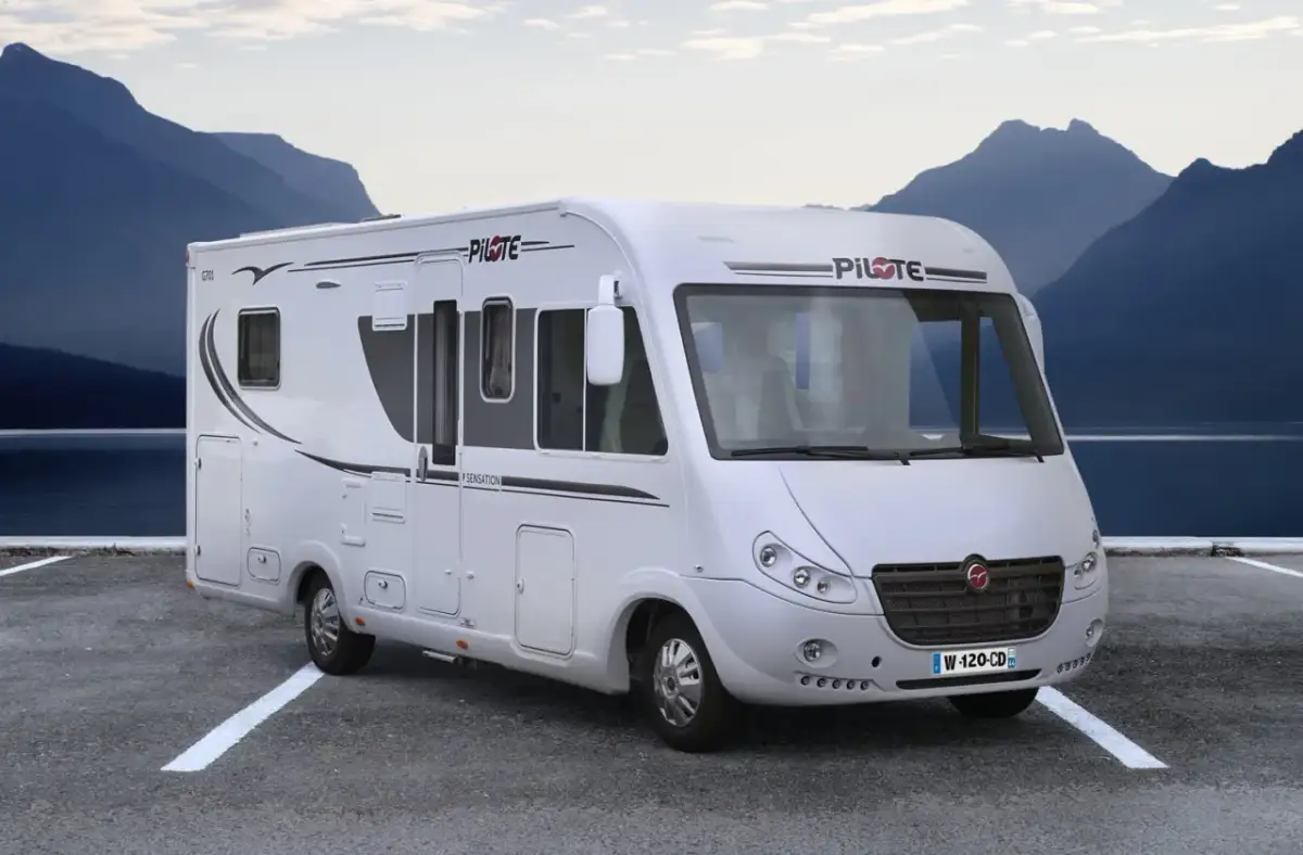 Biały kamper z prysznicem zaparkowany nad jeziorem, w tle góry.