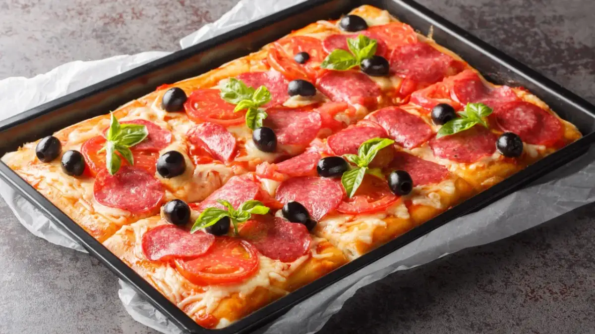 Chrupiąca pizza na cieście francuskim z salami, pomidorami i oliwkami, udekorowana listkami bazylii.