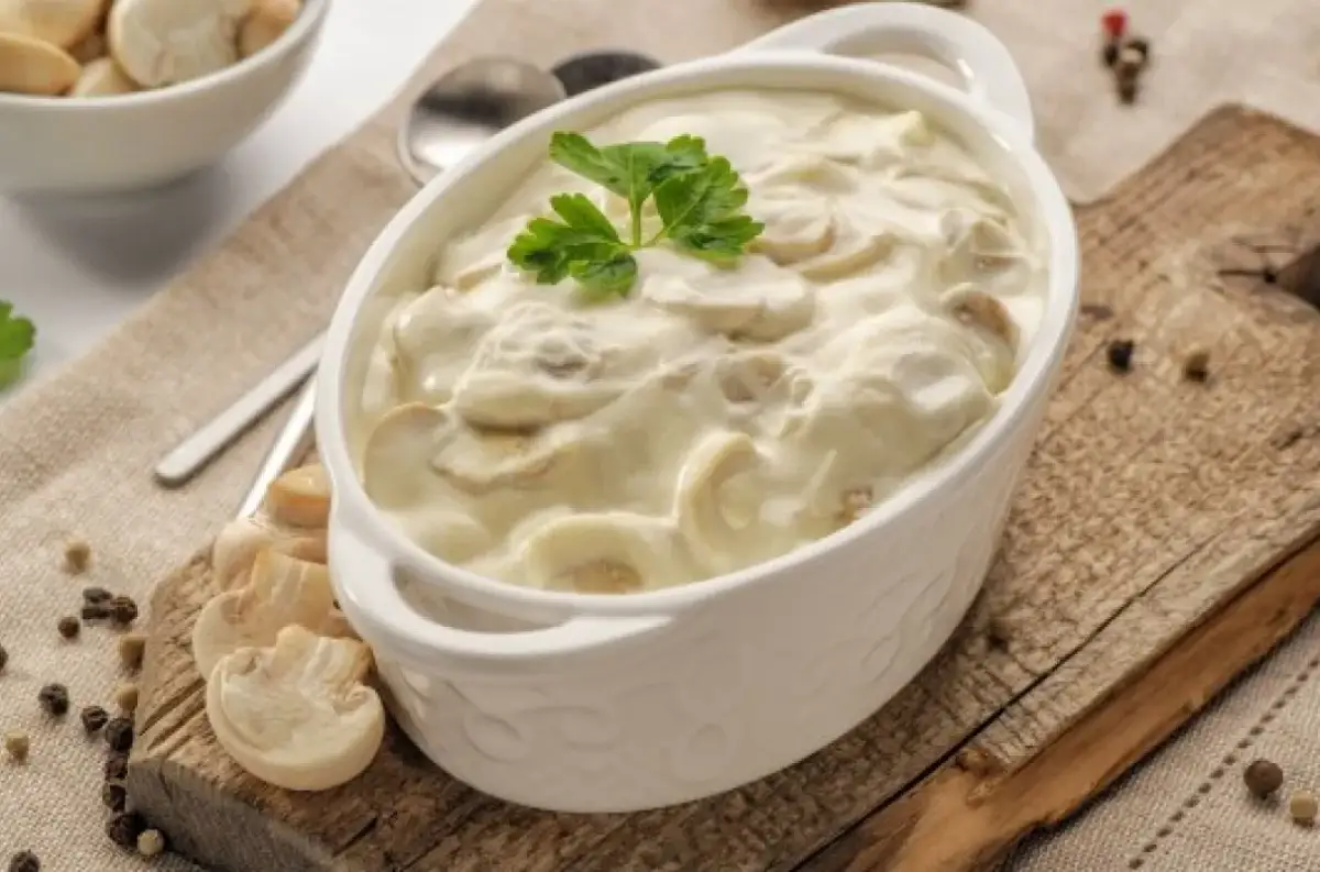 Pyszny, kremowy sos pieczarkowy w białej miseczce, udekorowany natką pietruszki. Idealny dodatek do obiadu.