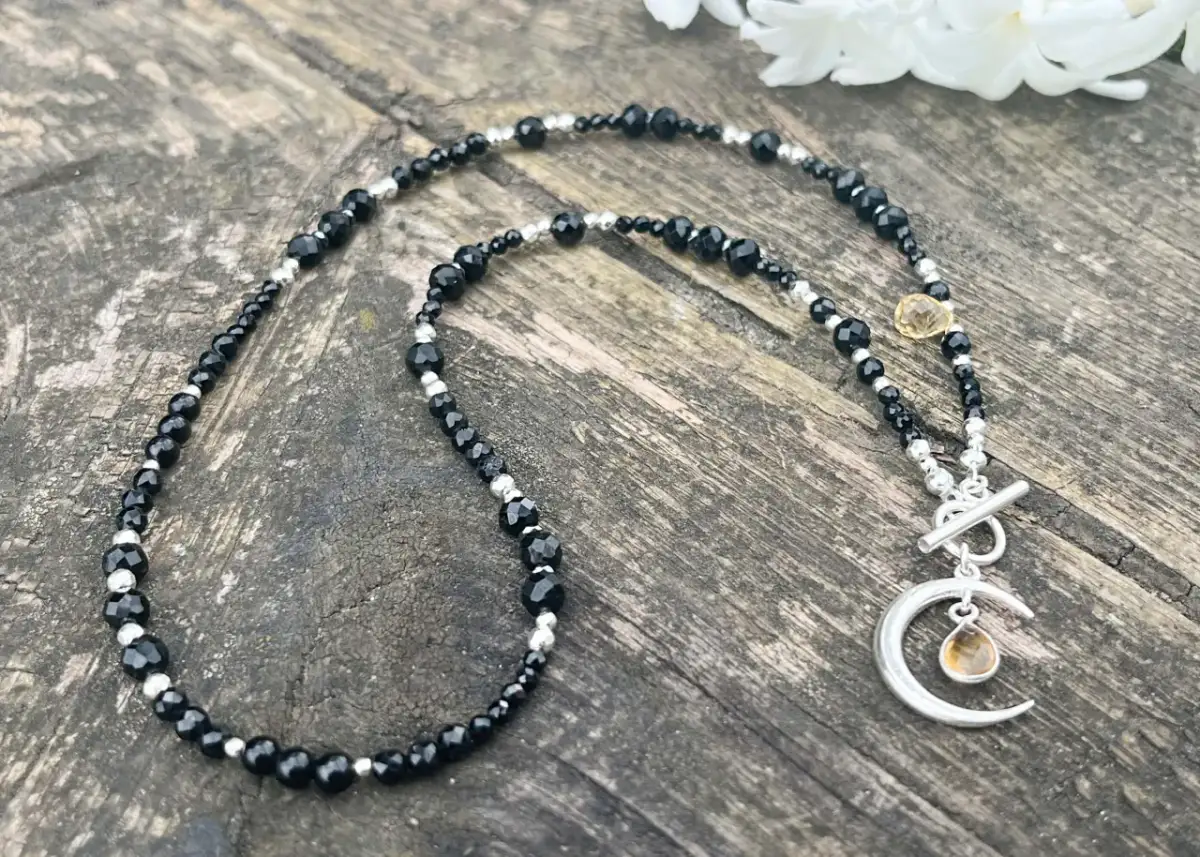 Naszyjnik z czarnych kamieni i srebrnych kuleczek z zawieszką w kształcie księżyca z bursztynowym kamieniem.