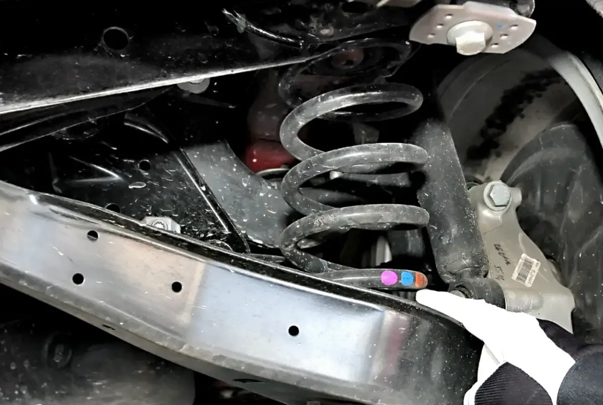 Widoczna pęknięta sprężyna w zawieszeniu auta. Objawy mogą obejmować stukanie, nierównomierne zużycie opon i obniżenie nadwozia.