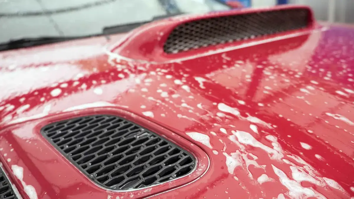 Czerwona maska samochodu pokryta pianą, przygotowana do glinkowania lakieru.