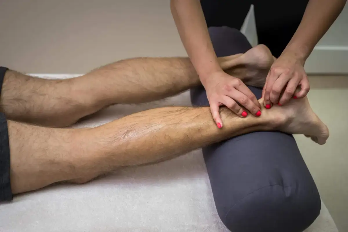 Fizjoterapeuta masuje stopę pacjenta, która jest podparta wałkiem.