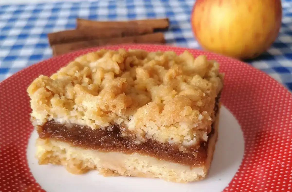 Pyszny kawałek szarlotki bez cukru z jabłkami i cynamonem, na talerzyku w kropki. Obok jabłko i laski cynamonu.