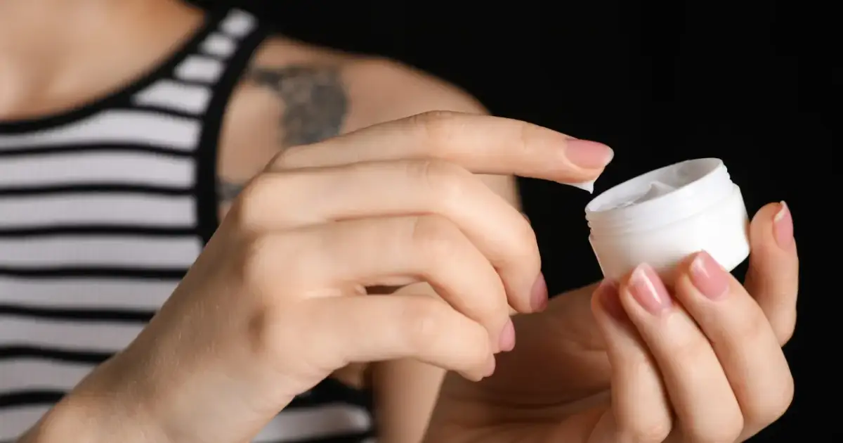 Dłonie nakładają krem z małego słoiczka. Odkryj tanie kosmetyki z apteki, które działają cuda dla Twojej skóry.