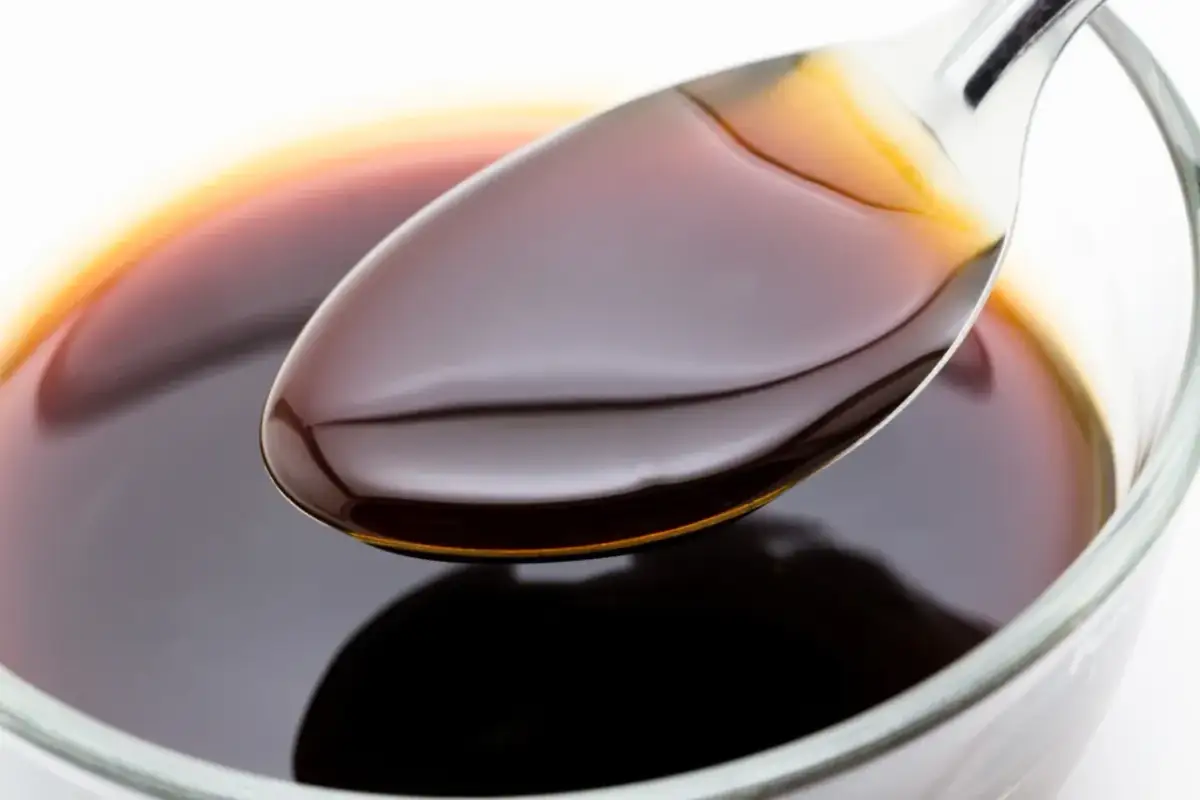 Łyżka z ciemnym, błyszczącym sosem sojowym nad miseczką. Czy sos sojowy jest zdrowy? Zależy od ilości i składu.