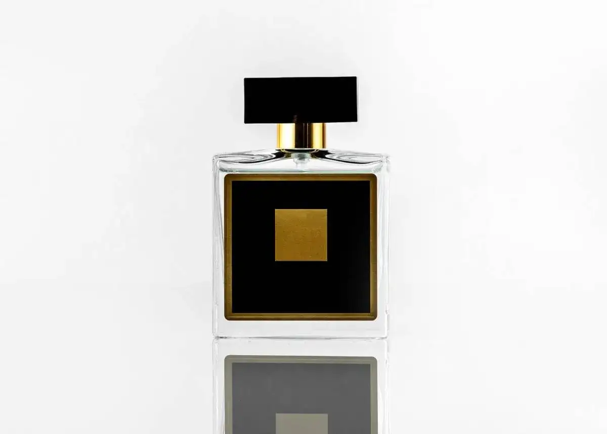 Elegancka szklana butelka perfum z czarną etykietą i złotym kwadratem.