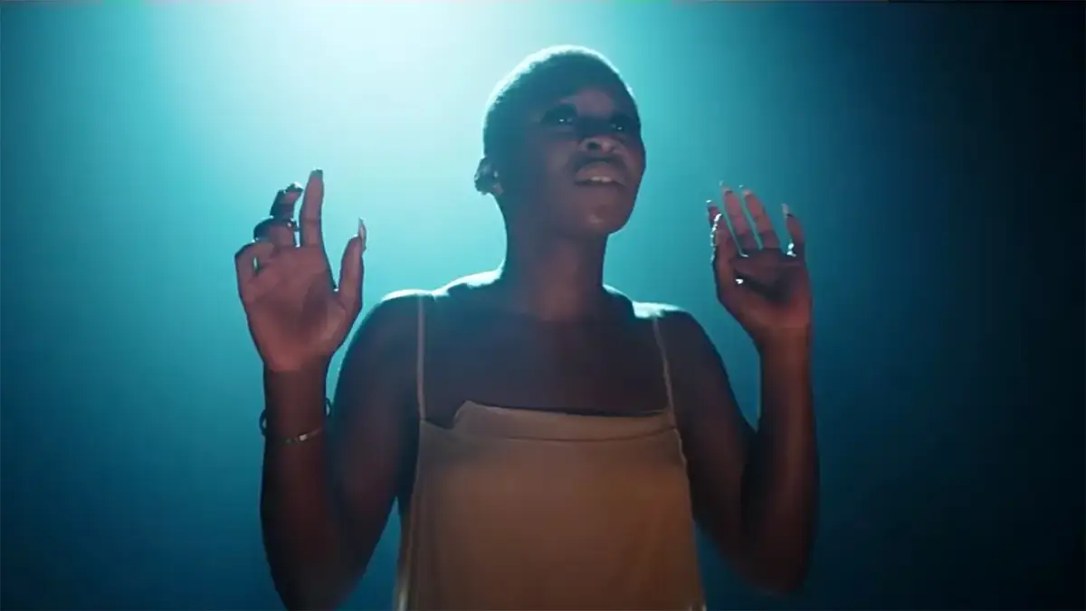 Cynthia Erivo stand up, wznosi ręce w górę, w świetle reflektorów.