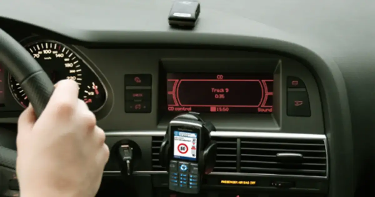 Ręka na kierownicy, telefon z nawigacją i ekran radia w samochodzie. Czy to podpowiedź, jak odkodować radio?