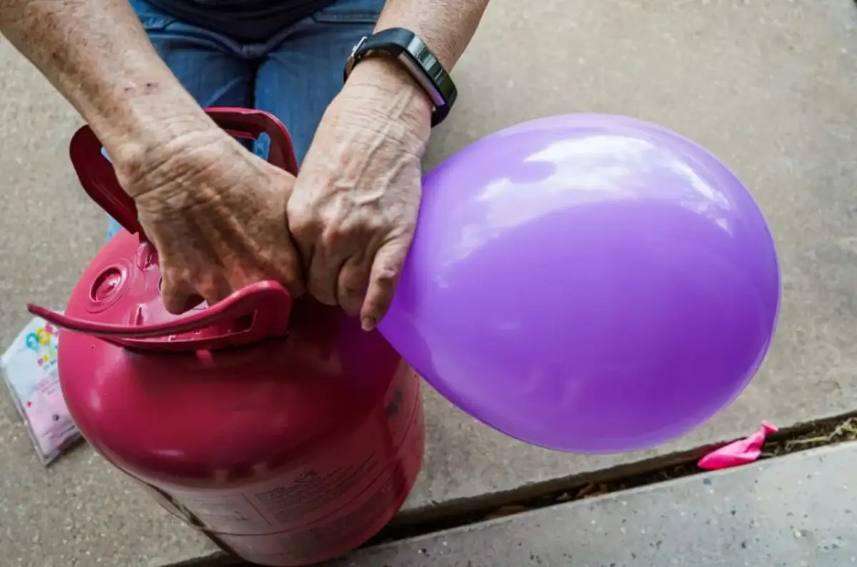Ręce nadmuchują fioletowy balon z butli z helem. Czy balony foliowe można nadmuchać powietrzem? Tak, ale ten balon jest foliowy i napełniany helem.