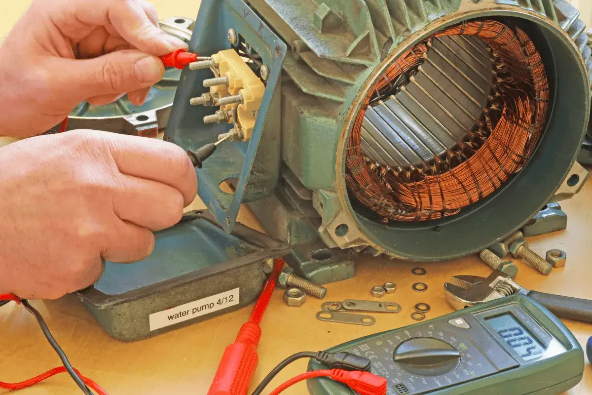 Ręce majsterkowicza sprawdzają uzwojenie silnika jednofazowego multimetrem.