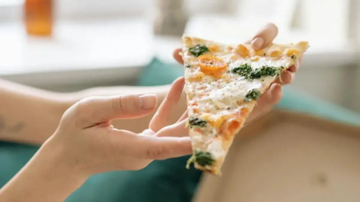 Kawałek pizzy z pomidorkami i szpinakiem, trzymany w dłoniach. Tak jeść pizzę we Włoszech – delektując się każdym kęsem.