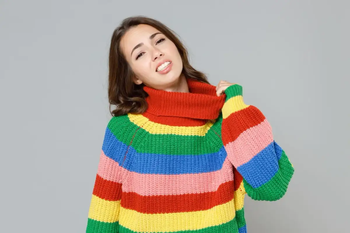 Dziewczyna w kolorowym golfie ciągnie za kołnierz, jakby zastanawiała się, co zrobić, gdy sweter gryzie.