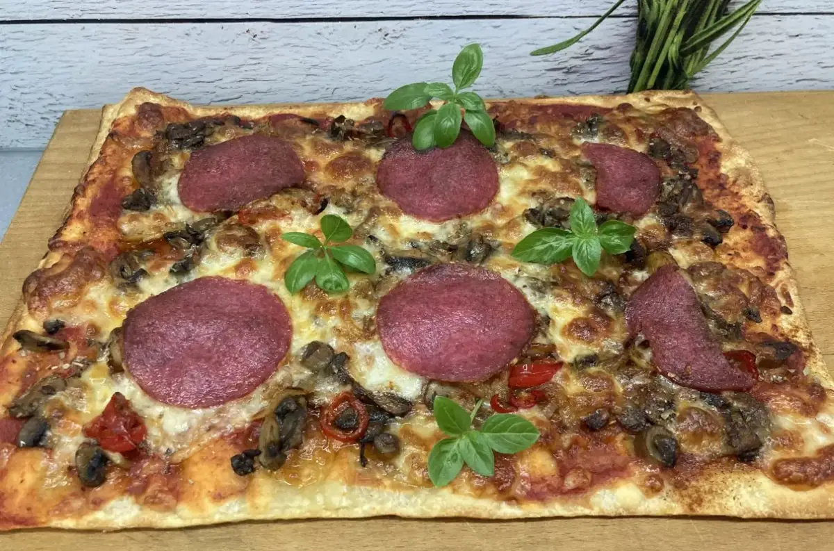 Prostokątna pizza z salami, pieczarkami i papryką, ozdobiona listkami bazylii. Idealne dodatki dla miłośników klasyki.