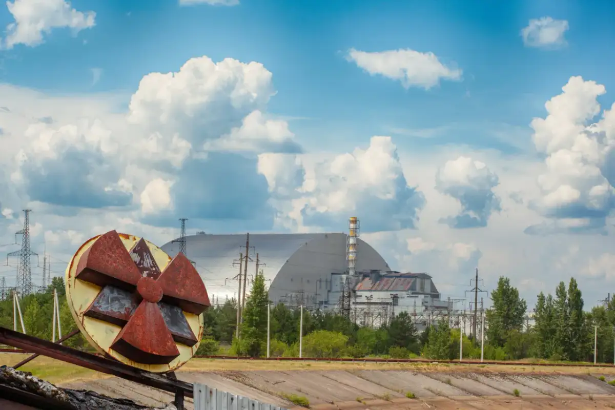 Rdzawe koło symbolizujące zagrożenie promieniotwórczością na tle sarkofagu Czarnobylskiej Elektrowni. Kiedy Czarnobyl będzie bezpieczny?